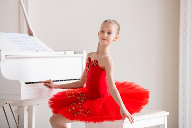 Une jolie petite fille rêve de devenir une ballerine professionnelle Dans une salle blanche, il se tient au piano dans un sac rouge vif Élève de l'école professionnelle