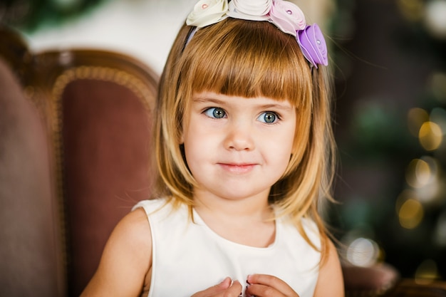 Jolie petite fille à la robe blanche avec une belle couronne près du sapin de Noël