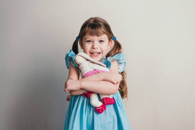 Jolie petite fille en robe bleue et embrasse son lapin jouet