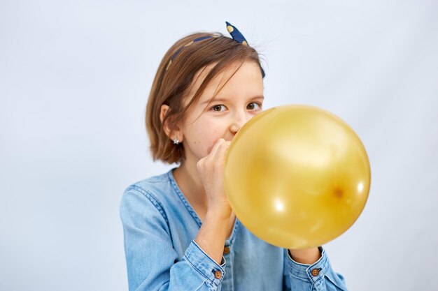 Jolie petite fille en robe denim décontractée soufflant gonfler un ballon jaune