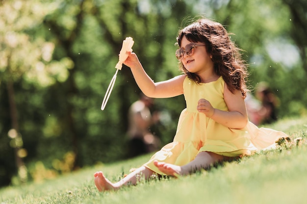 jolie petite fille en robe jaune jouant avec des bulles dans le parc