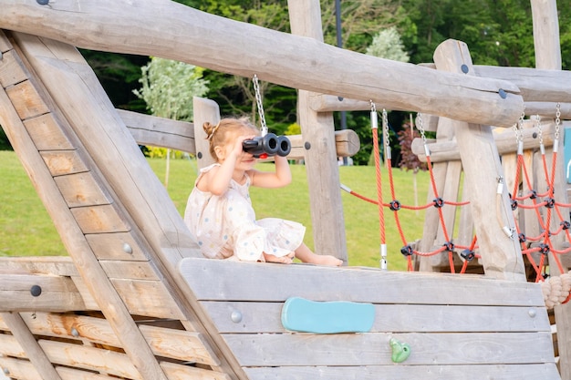 jolie petite fille en robe jouant sur l'aire de jeux pour enfants en été