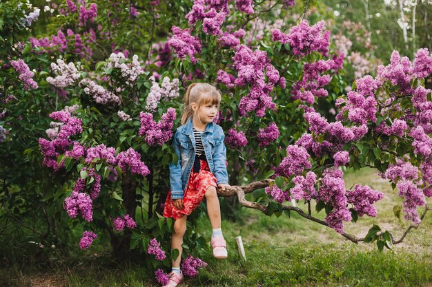 Jolie petite fille en robe riant dans le parc du printemps près de l'enfant lilas sent le lilas