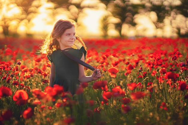 Jolie petite fille en robe verte posant au champ de coquelicots sur coucher de soleil d'été