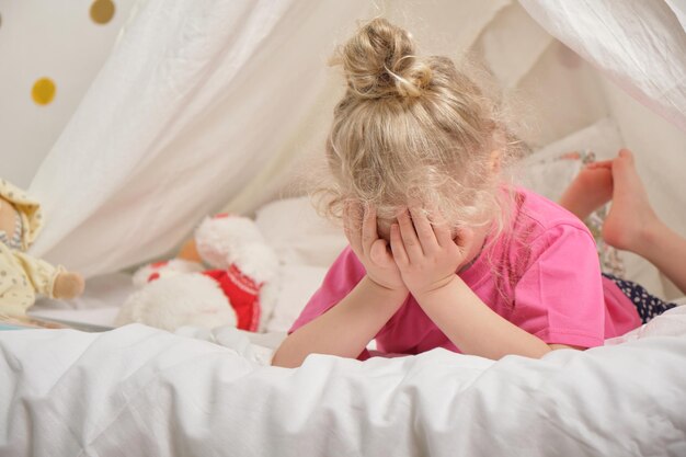 Jolie petite fille s'amusant et jouant dans sa tente, Hutte dans la chambre des enfants, activités concep la fille a couvert son visage avec ses mains en position couchée sur le lit