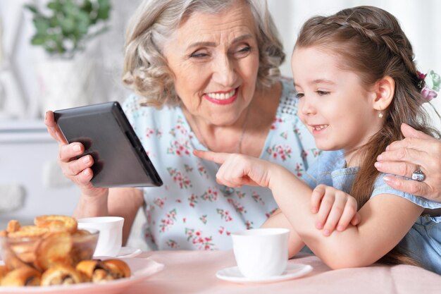 Jolie petite fille avec sa grand-mère regardant une tablette à la maison