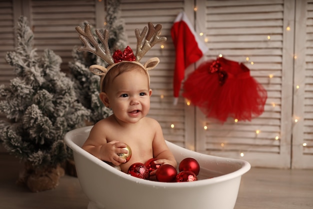 une jolie petite fille se baigne dans une baignoire avec des jouets d'arbre de Noël rouge et or la fille est heureuse