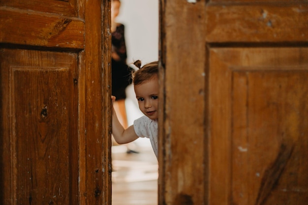 Une jolie petite fille se cachant derrière une grande porte en bois regardant dans l'espace entre eux effet de bruit de mise au point sélective