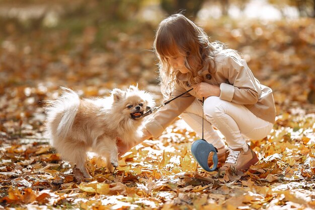 Une jolie petite fille se promène dans un parc d'automne avec un chien.