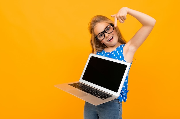 Jolie petite fille avec ses lunettes est titulaire d'un ordinateur portable et sourit isolé sur mur blanc