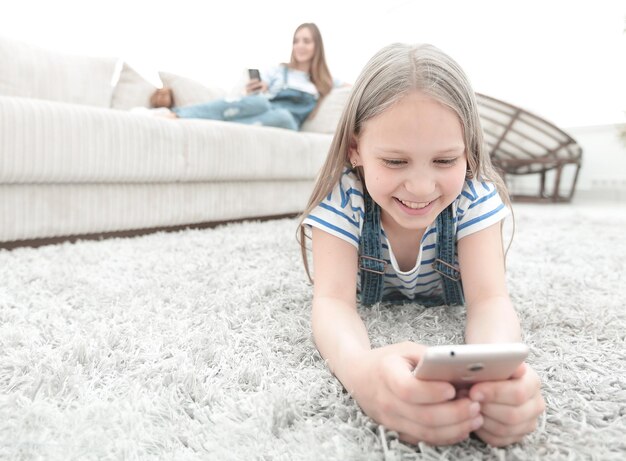 Jolie petite fille avec smartphone allongé sur le tapis dans le salon