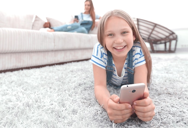 Jolie petite fille avec un smartphone allongé sur le tapis dans le salonphoto avec espace de copie