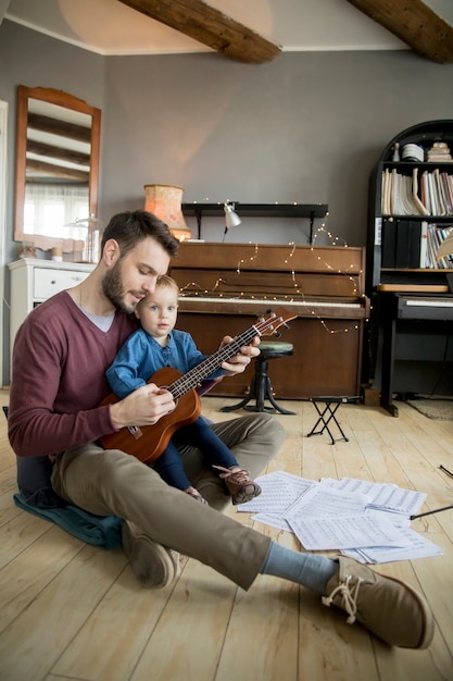 Jolie petite fille et son beau père jouent de la guitare et souriant assis dans la chambre