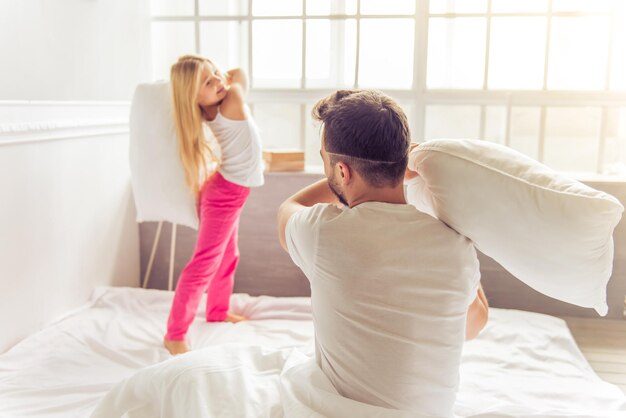 Jolie petite fille et son père se battent avec des oreillers et sourient assis sur le lit à la maison