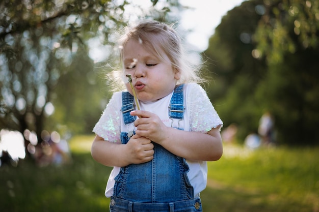 Jolie petite fille soufflant des graines de pissenlit au coucher du soleil dans le parc d'été Image avec mise au point sélective