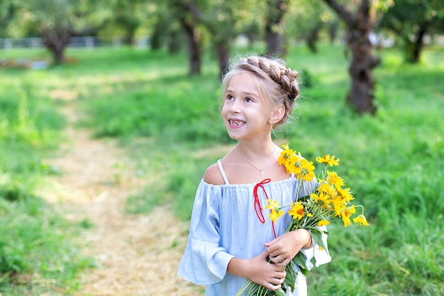 jolie petite fille souriante avec bouquet de fleurs jaunes dans le jardin d'été enfant avec marguerites