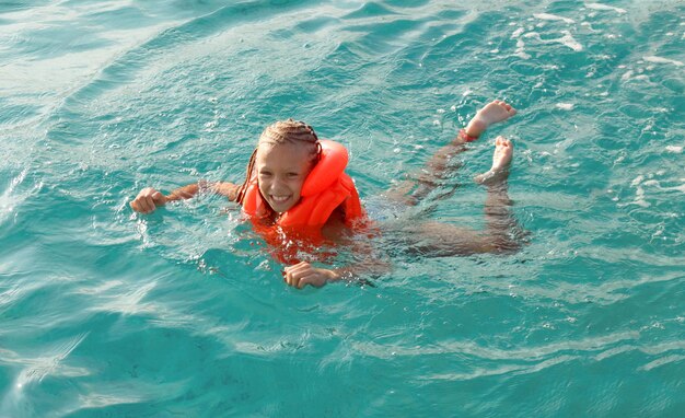 Jolie petite fille souriante avec gilet de bain profitant d'une baignade détendue dans la mer.