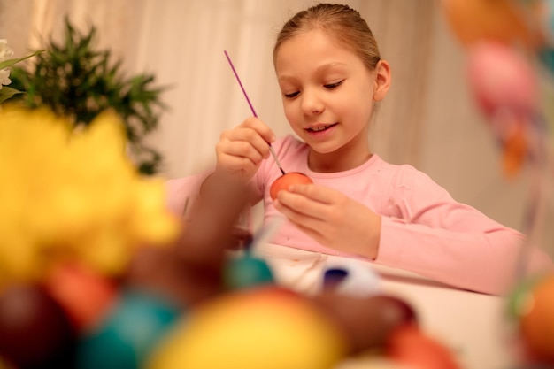 Jolie petite fille souriante peignant l'oeuf de Pâques à la maison.