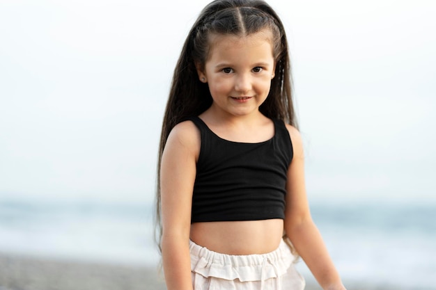 Une jolie petite fille souriante posant sur la plage en regardant la caméra Concept d'été de vacances de voyage