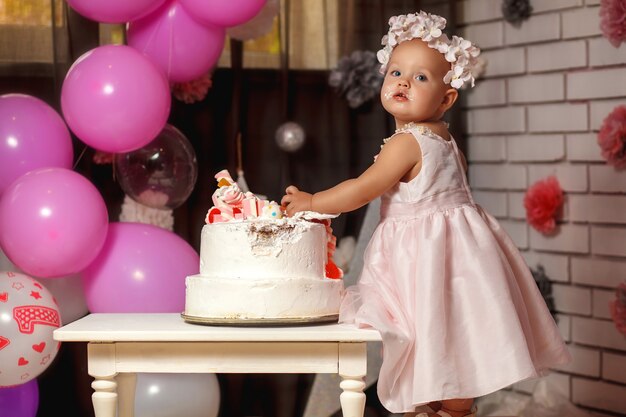 Jolie petite fille souriante en robe rose avec son premier gâteau d'anniversaire