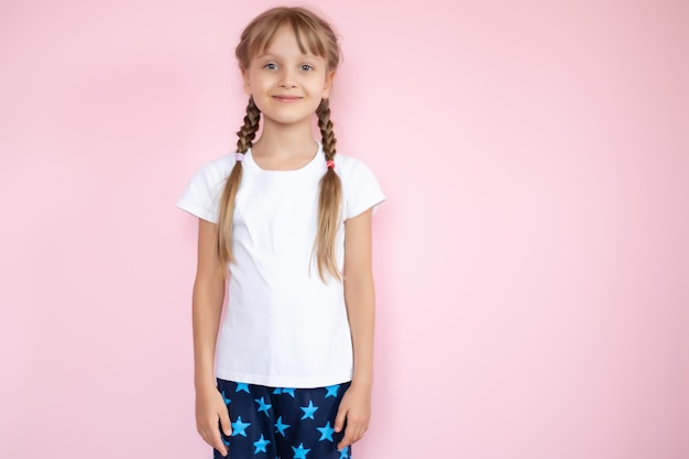 Jolie petite fille en t-shirt blanc souriant sur fond rose