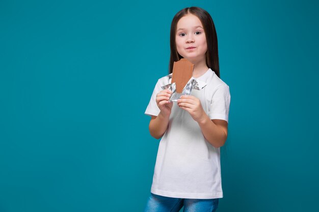 Jolie petite fille en tee-shirt avec de longs cheveux, avec une barre chocolatée dans les mains