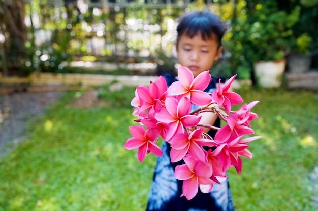 Jolie petite fille tenant un bouquet de fleurs de frangipanier dans le jardin