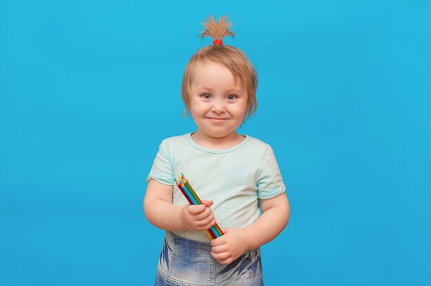 Jolie petite fille tenant des crayons colorés en regardant la caméra Isoler sur fond bleu