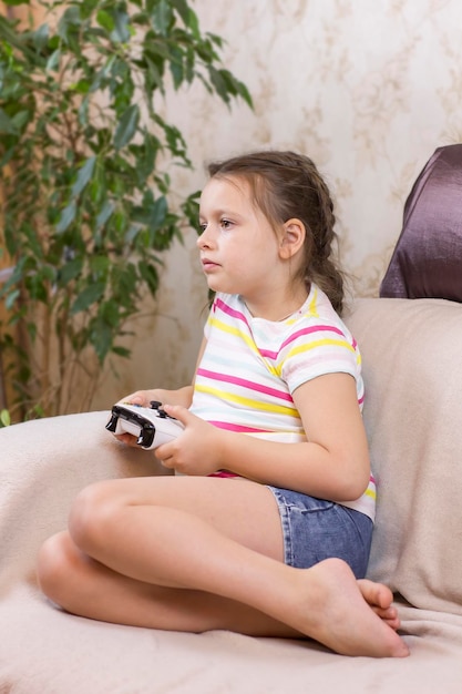 Jolie petite fille tenant un joystick et jouant à un jeu vidéo sur un canapé à la maison