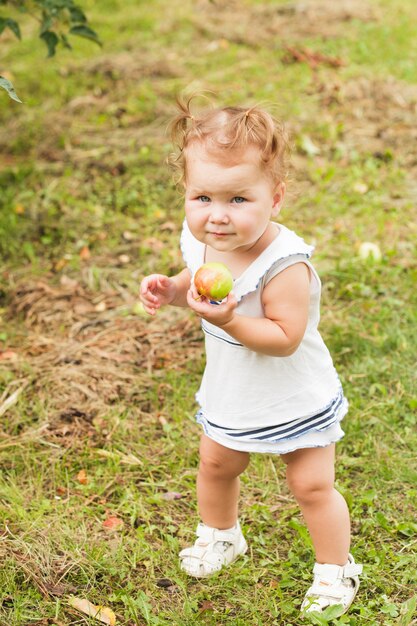 Jolie petite fille tenant une pomme à la main, debout sous le pommier