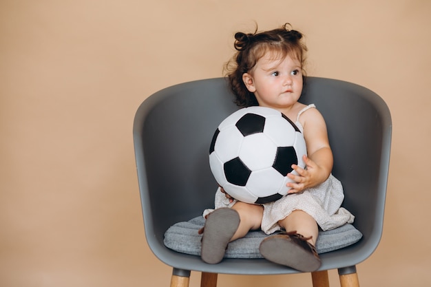 Une jolie petite fille tient le ballon, regarde le football et encourage son équipe