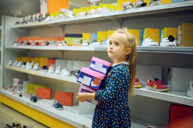 Jolie petite fille tient une boîte avec des chaussures dans un magasin pour enfants