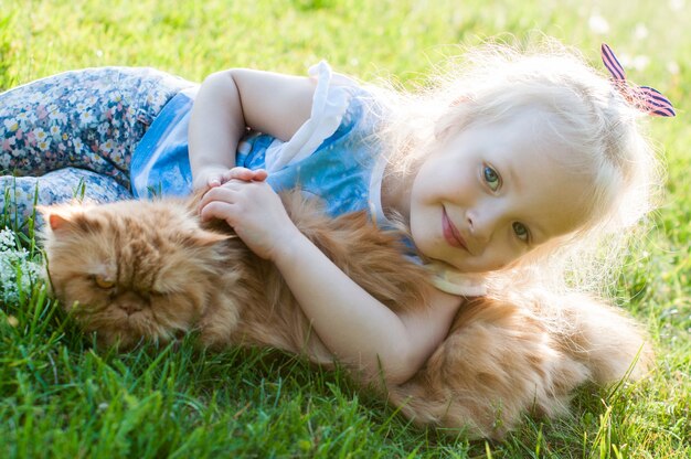 Jolie petite fille tient un chat rouge dans la nature assis dans l'herbe