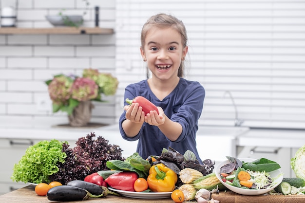 Une jolie petite fille tient des légumes frais tout en préparant un espace de copie de salade.