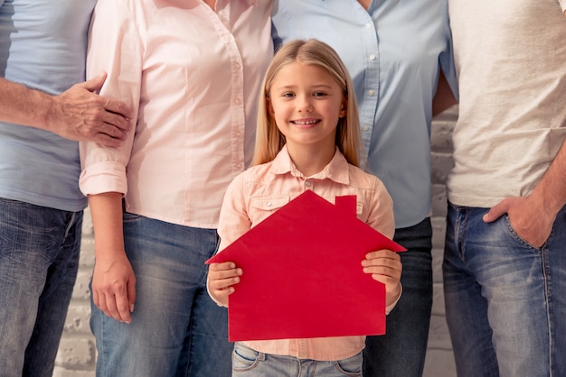 Jolie petite fille tient une maison de papier en regardant la caméra.