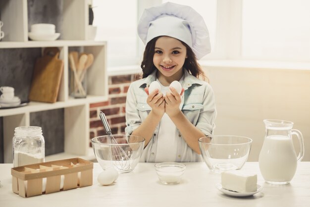 Jolie petite fille en toque tient des oeufs.