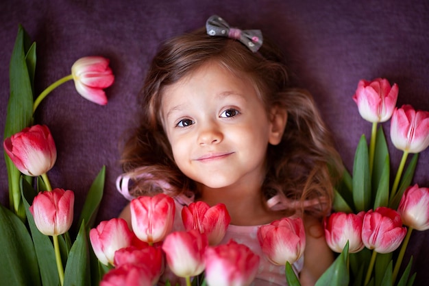 une jolie petite fille avec des tulipes est allongée sur une couverture violette et souriante