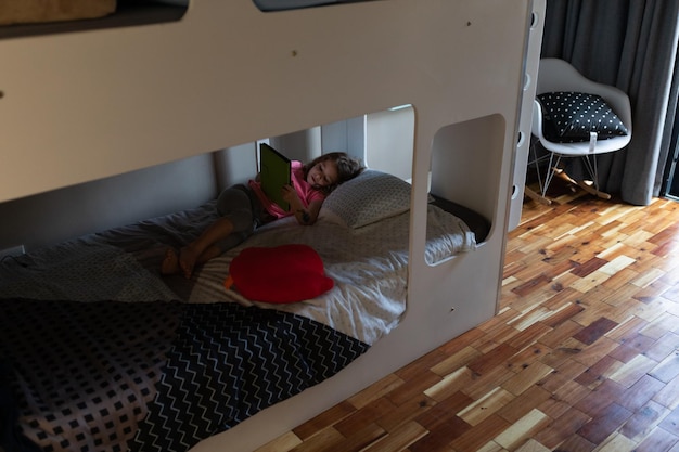 Photo une jolie petite fille utilisant une tablette numérique sur le lit dans la chambre à coucher à la maison