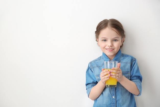 Jolie petite fille avec un verre de jus sur un mur blanc avec espace de copie