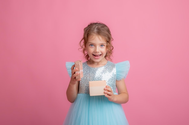 Une jolie petite fille vêtue d'une belle robe tient la baguette magique d'une fée et un cadeau sur fond rose