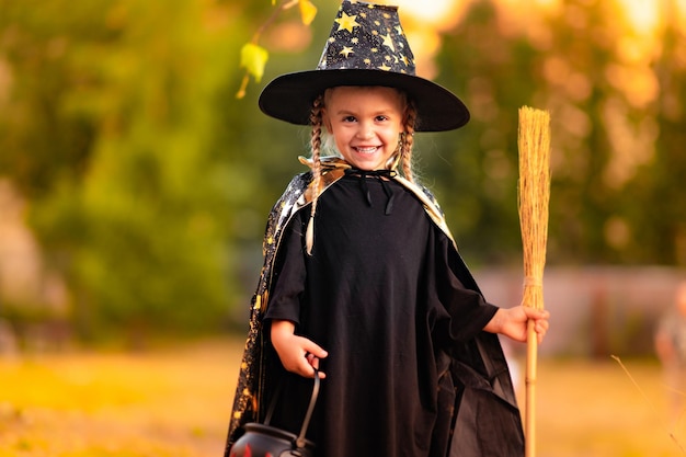 Photo jolie petite fille vêtue d'un costume de sorcière célébrant dans le parc tenant un bol de bonbons à la main