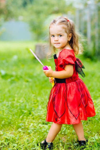 Jolie petite fille vêtue d'une longue robe rouge jouant et s'amusant sur une pelouse verte
