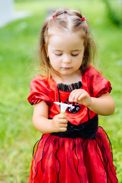 Jolie petite fille vêtue d'une longue robe rouge jouant et s'amusant sur une pelouse verte