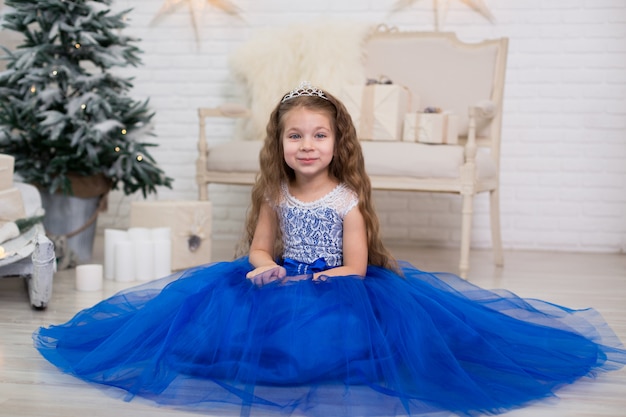 Jolie petite fille vêtue d'une robe bleue luxuriante posant près de l'arbre de Noël.