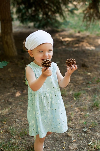 Une jolie petite fille vêtue d'une robe légère se promène dans le parc et ramasse des cônes Vacances d'été Enfance
