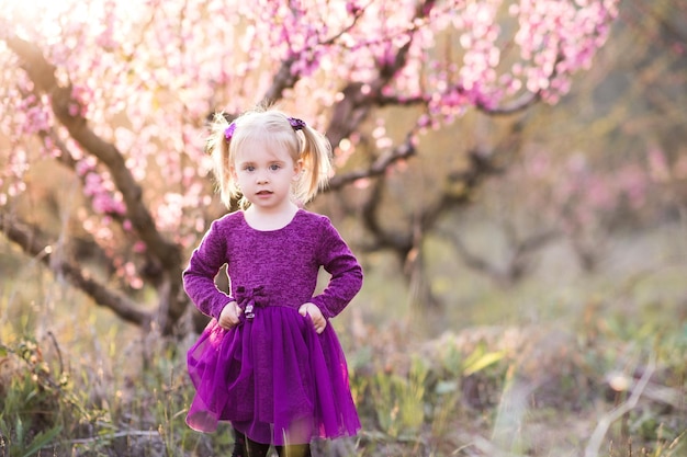 Jolie petite fille vêtue d'une robe violette debout sur une pêche en fleurs