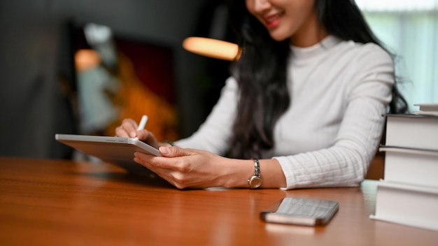 Jolie pigiste asiatique utilisant sa tablette assise à sa table de travail à domicile