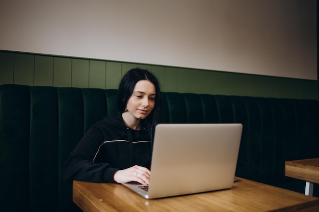 Une jolie pigiste discutant avec ses amis tout en étant assise devant un ordinateur ouvert dans un café vintage