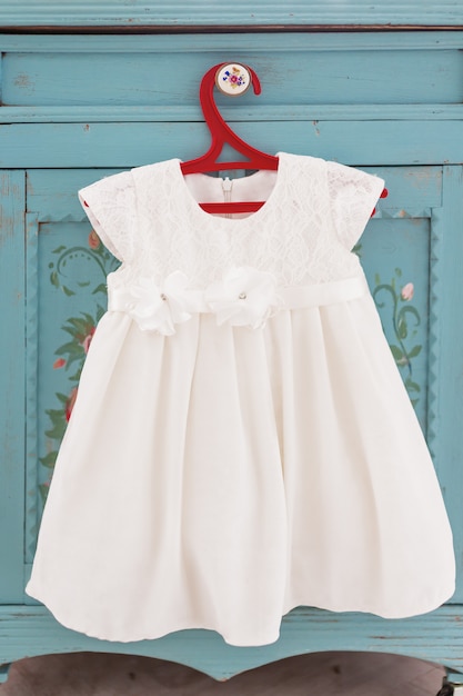 Jolie robe blanche lacée sur cintre rouge. Petite tenue de fille avec des fleurs décoratives.