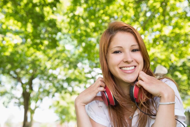 Jolie rousse écoutant de la musique dans le parc par une journée ensoleillée